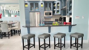 Uma cozinha moderna com uma ilha central, banquetas e uma área de jantar com cadeiras.