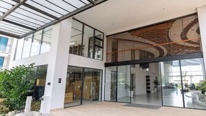 Un edificio moderno con grandes ventanales, techo de listones de madera y un espacio exterior cuidado con plantas.