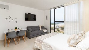 Un dormitorio moderno con cama, sofá gris, escritorio con sillas y televisor en la pared.