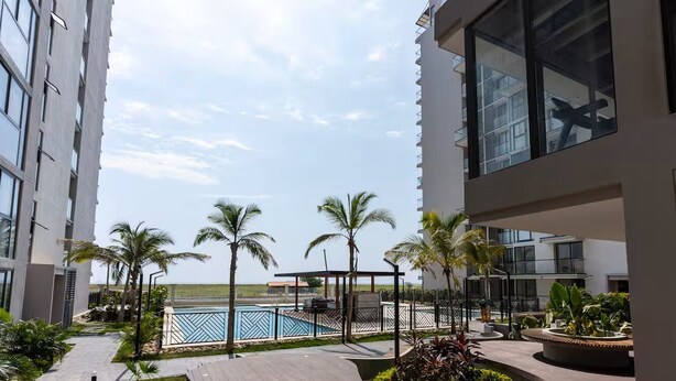 Un hotel moderno con zona de piscina, palmeras y vista despejada a la playa.