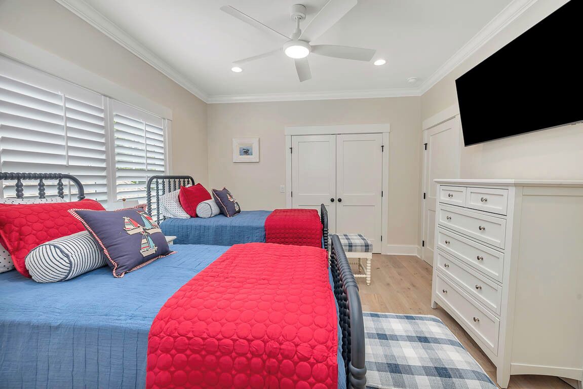 A bedroom with two beds, a ceiling fan, a TV, and a dresser.