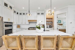 A modern kitchen with white cabinetry, a central island with seating, and stainless steel appliances. - COASTAL ESCAPE! Private Pool, Putting Green, & Short Walk to the Beach! (St. Simons Island)