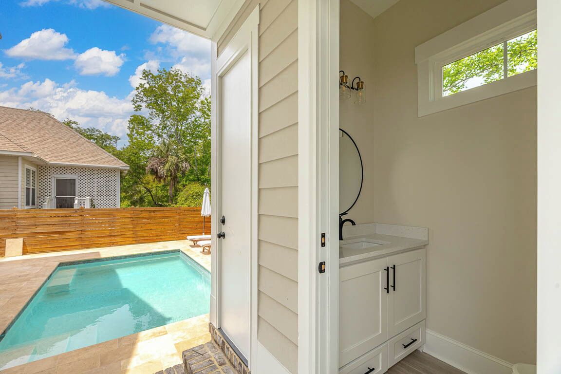 A bathroom with a white vanity, a shower, and a window with a view of a backyard swimming pool.
