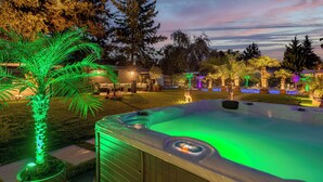 A hot tub with green lighting, surrounded by trees and a well-lit backyard. - Villa Tropicana (Teltow)