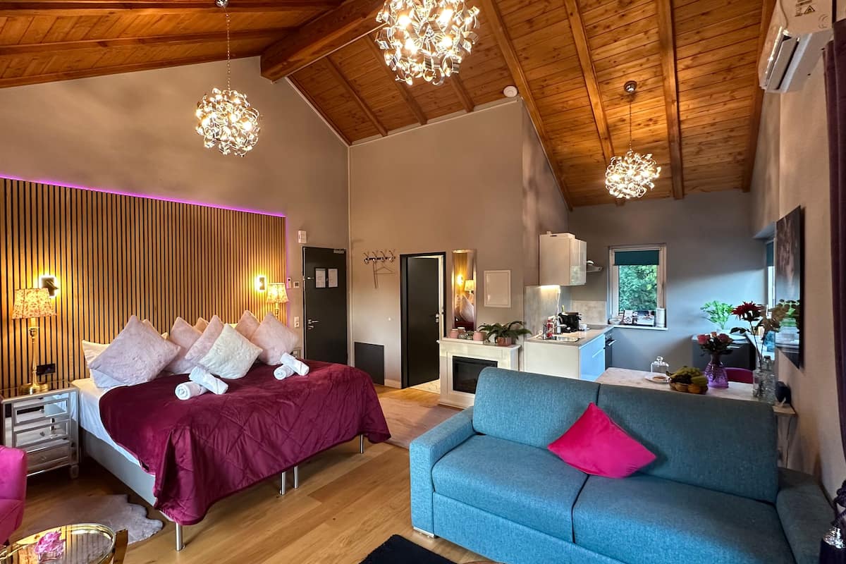 A modern bedroom with a large bed, a blue sofa, and a wooden ceiling.