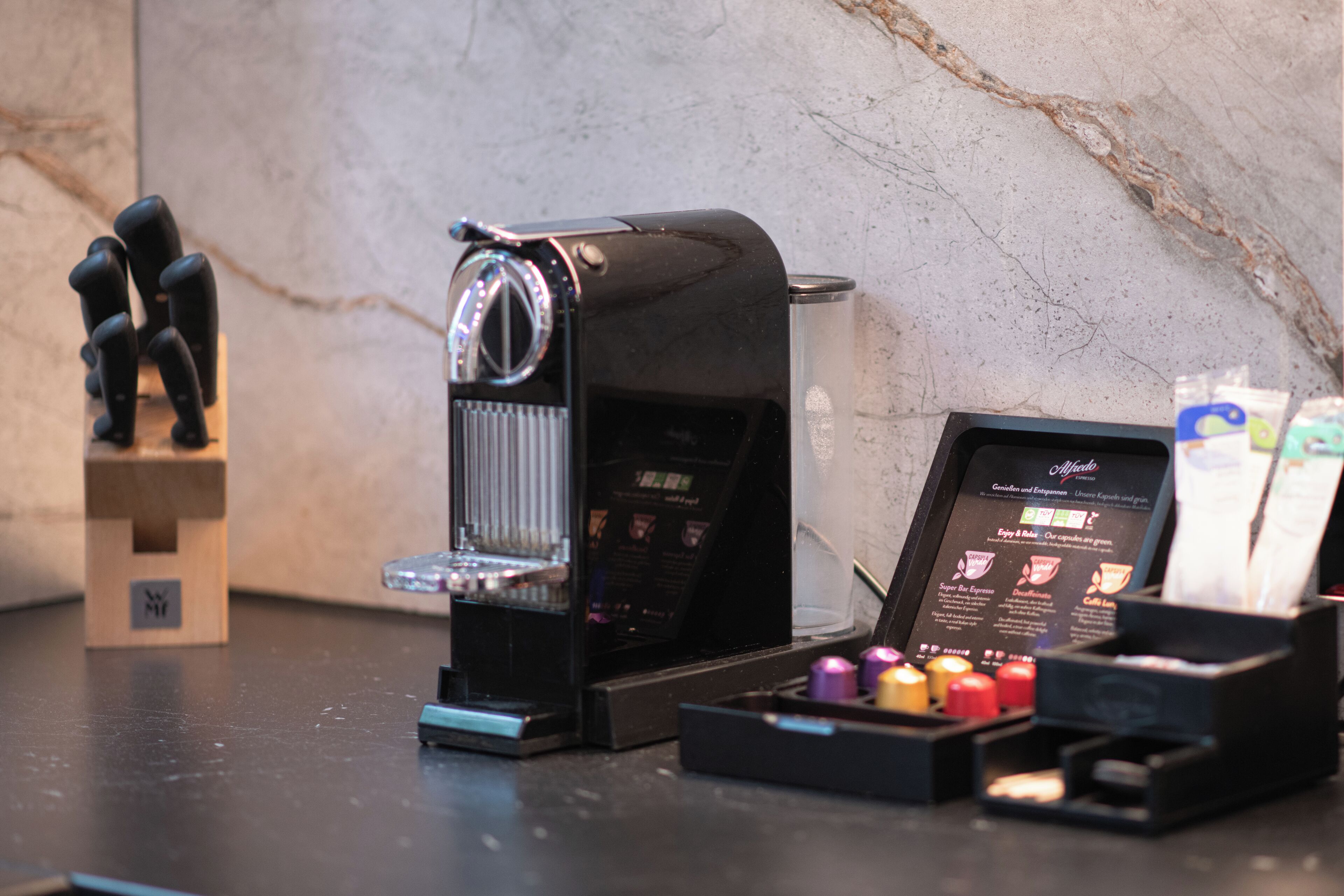 A coffee machine with a menu display, a coffee grinder, and a box of coffee pods on a marble countertop.