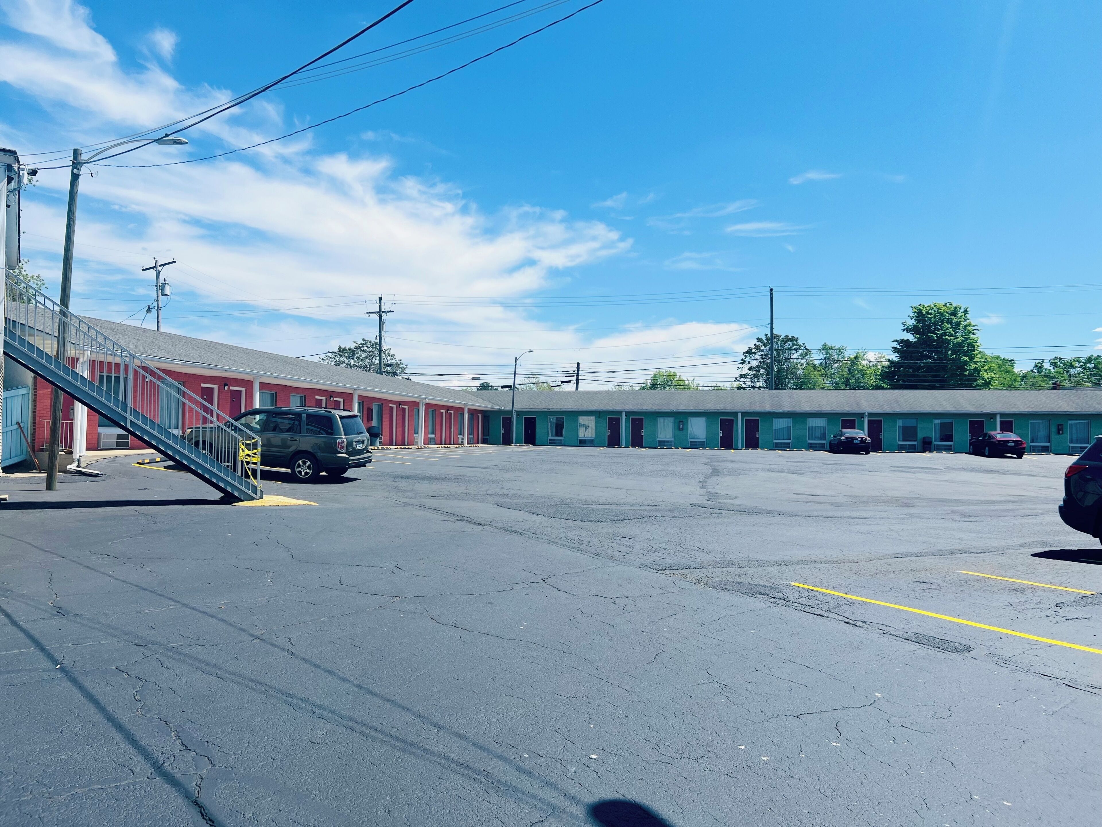 A motel with a parking lot, a staircase, and a row of rooms.