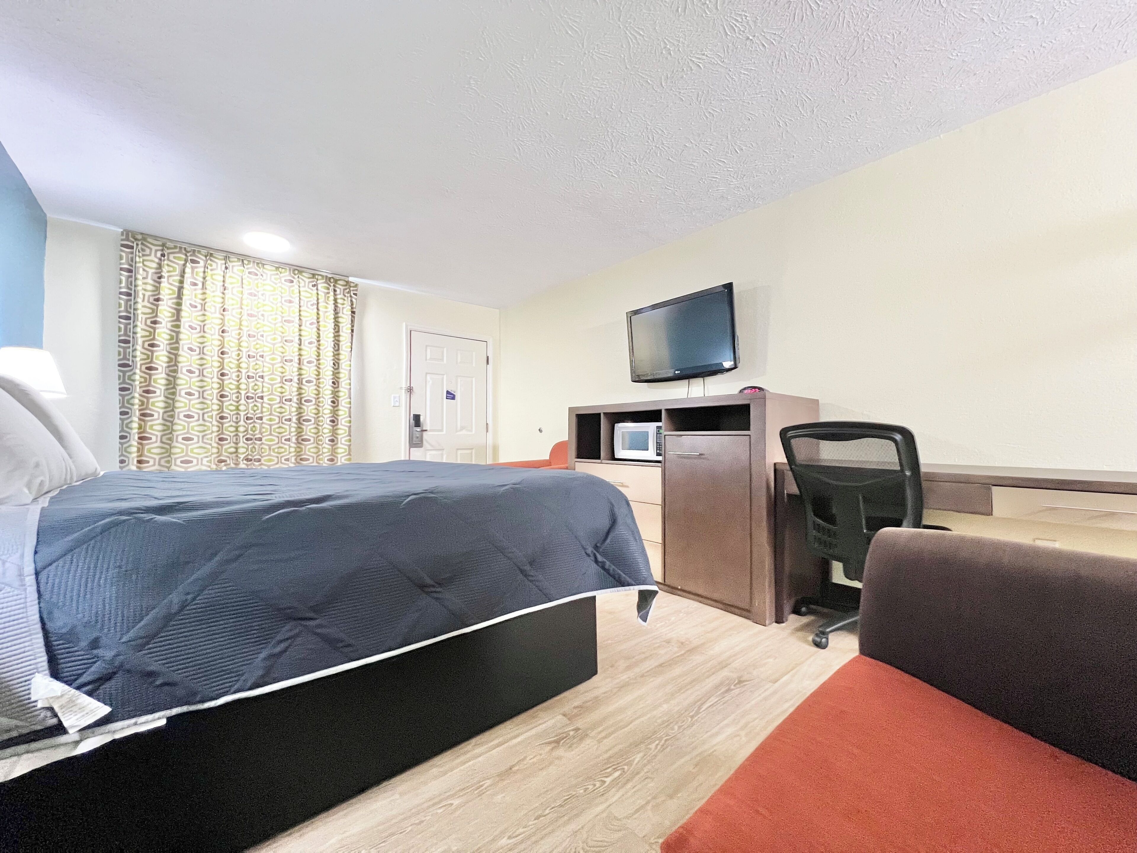 A hotel room with a bed, desk, chair, television, and a door.