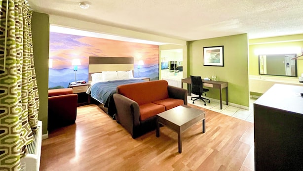 A hotel room with a bed, a sofa, a desk, and a chair. - Hometown INN (Berea)