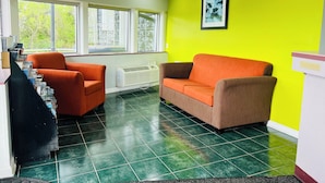 A room with two orange chairs, a white radiator, a TV mounted on the wall, and a window with a view of trees. - Hometown INN (Berea)