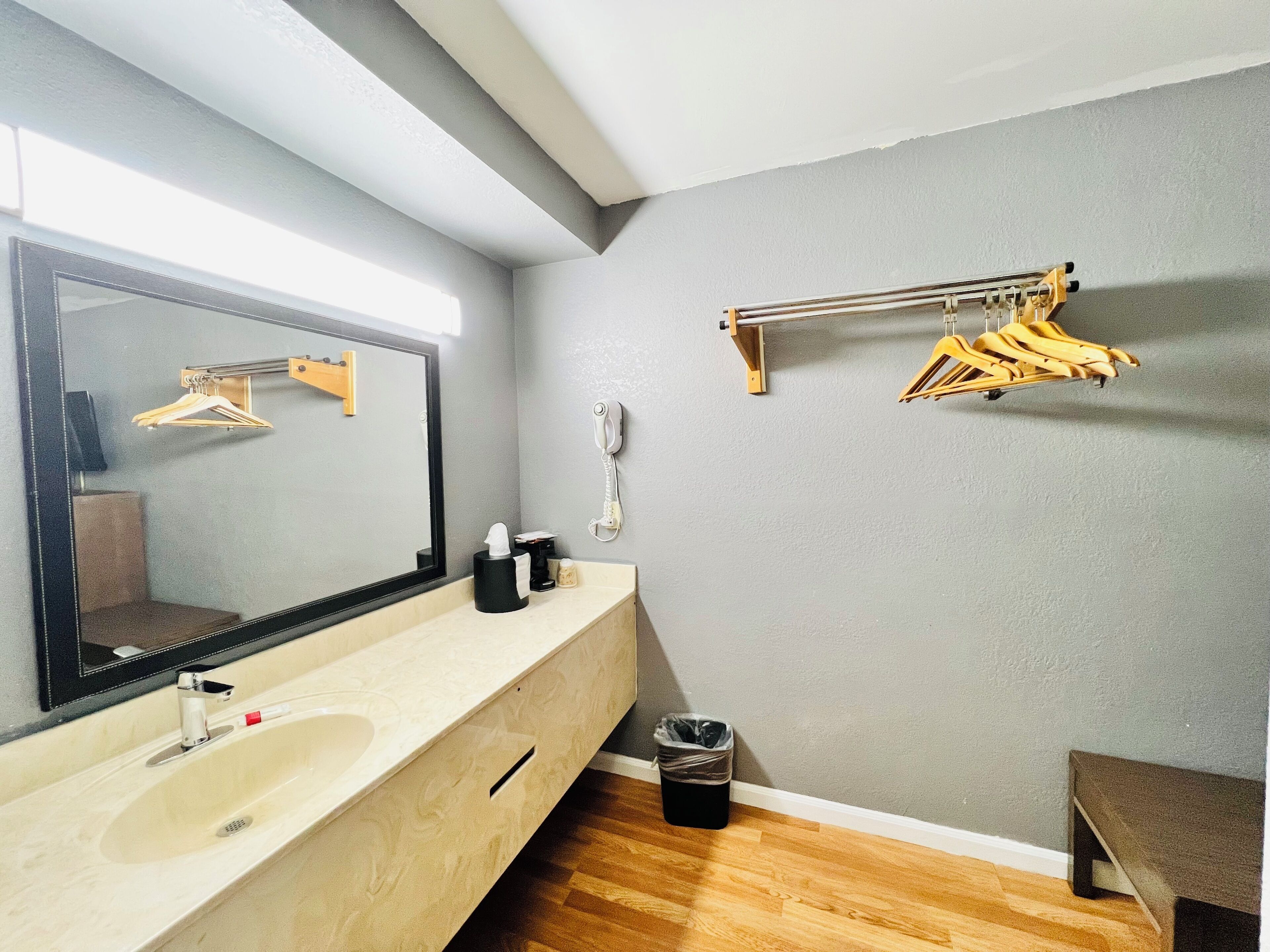 A bathroom with a large mirror, a sink, a telephone, and a clothes drying rack.