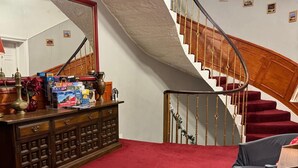 A living room with a red carpet, a wooden cabinet, a sofa, and a staircase with a wooden railing. - Sofia Rooms (Edinburgh)
