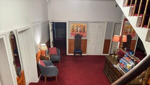 A room with a red carpet, two armchairs, a wooden cabinet with magazines, and a staircase with a wooden railing. - Sofia Rooms (Edinburgh)