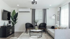 A modern living room with a sofa, two armchairs, a coffee table, a TV, and a large plant.