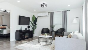 A modern living room with a sofa, two armchairs, a coffee table, a TV, and a black entertainment unit.