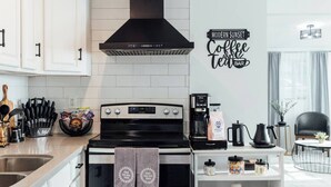A modern kitchen with a stove, coffee maker, and a wall sign that reads "Modern Sunset Coffee and Tea Bar".