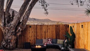 A cozy outdoor seating area with a fire pit, wooden walls, and a large tree.