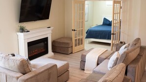 Una sala de estar con chimenea, un televisor montado encima y una cama en la habitación contigua.