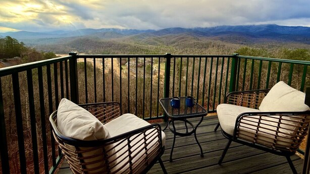 A balcony with wicker chairs and a small table, overlooking a mountainous landscape. - Vista Ridge Retreat at Deer Ridge Mountain Resort (Gatlinburg)