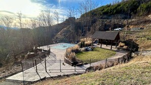 A fenced outdoor area with a pool, a small building, and a hilly landscape in the background. - Vista Ridge Retreat at Deer Ridge Mountain Resort (Gatlinburg)