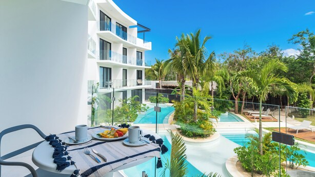 Un balcon aménagé avec un coin repas donnant sur une piscine, comprenant une table avec des assiettes, des tasses et des couverts.