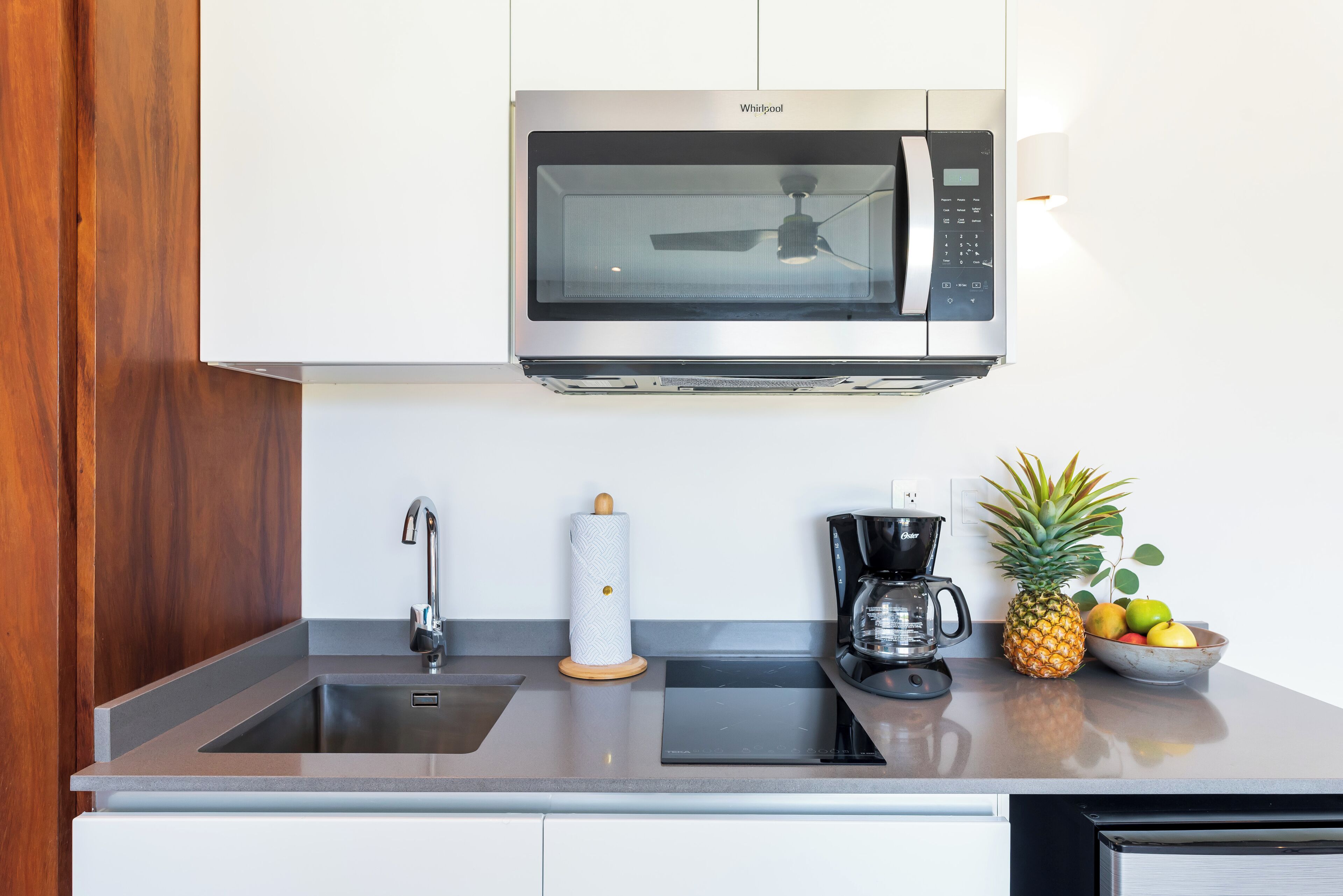 A modern kitchen with a built-in microwave, a coffee maker, and a bowl of fruit on the counter.