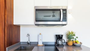Une cuisine moderne équipée d’un four à micro-ondes encastré, d’une machine à café et d’un saladier rempli de fruits posé sur le plan de travail.