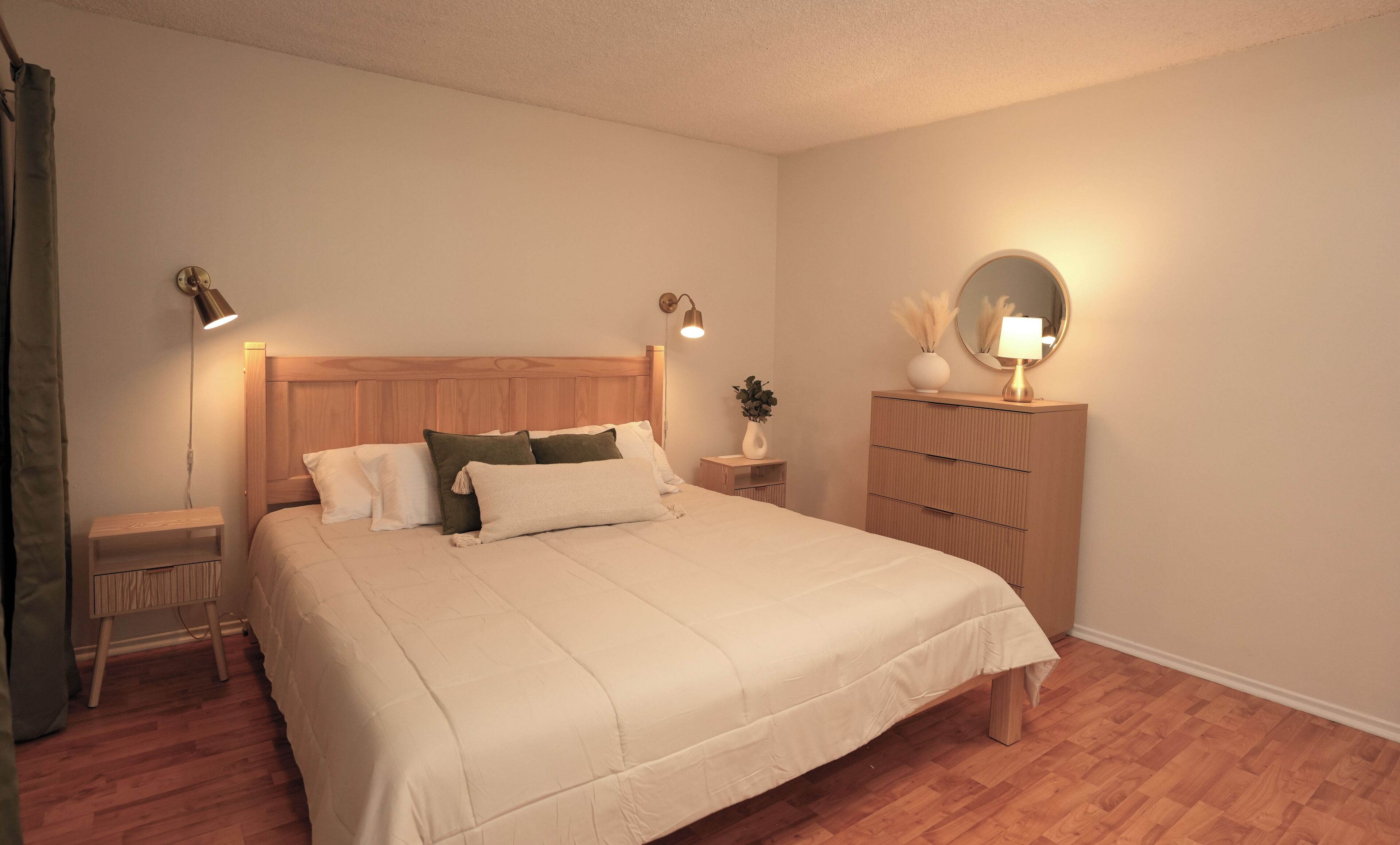 Un dormitorio ordenado con una cama de tablero de madera, mesitas de noche con lámparas, un aparador y un espejo.