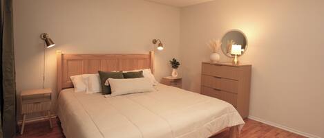 Un dormitorio ordenado con una cama de tablero de madera, mesitas de noche con lámparas, un aparador y un espejo.