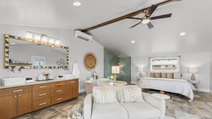 Une chambre spacieuse avec un grand lit, un coin salon avec un canapé, une coiffeuse avec un miroir et un ventilateur de plafond.