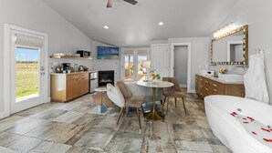 A spacious living area with a round dining table, comfortable seating, a fireplace, and a large window offering a view of the outdoors.