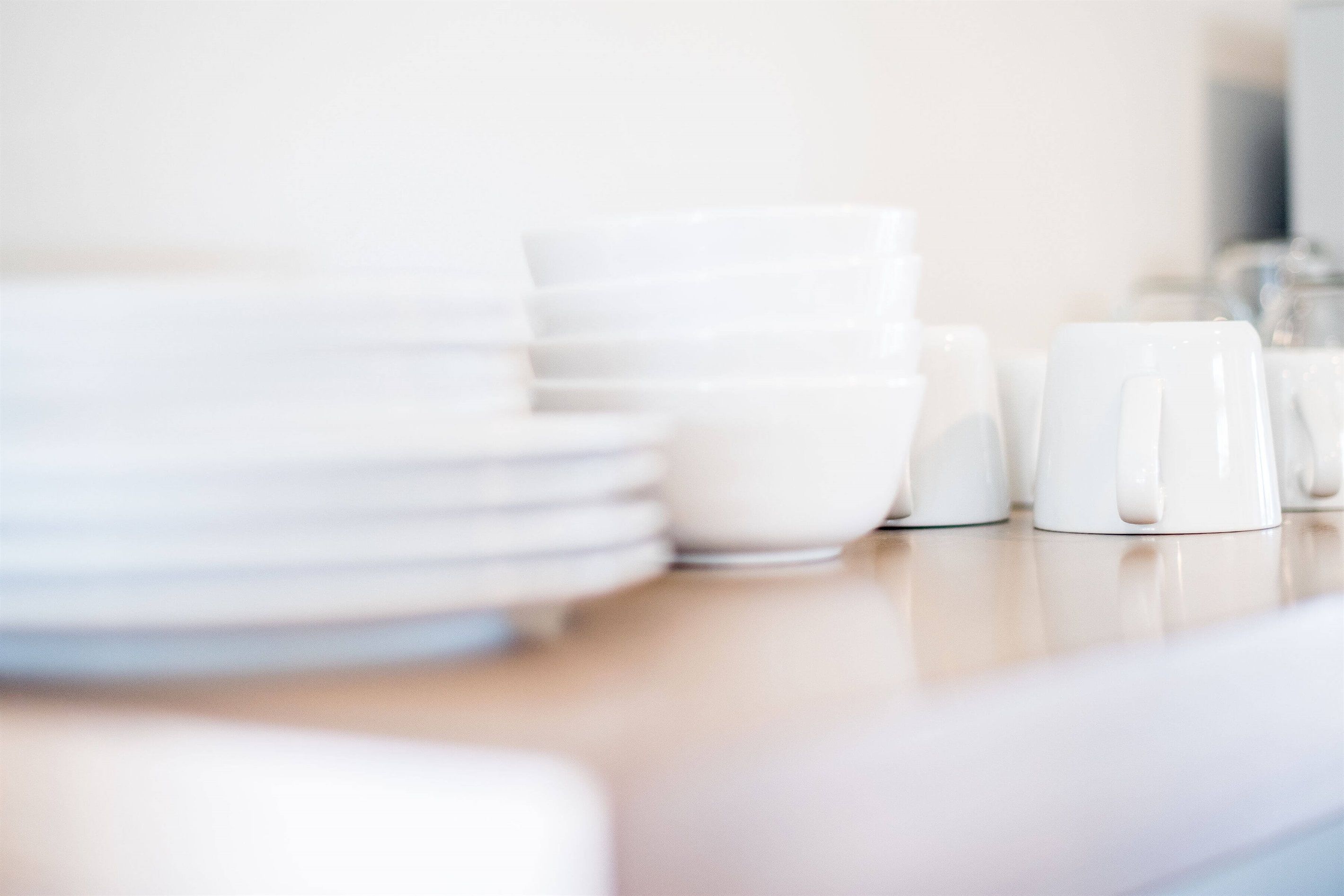A stack of white plates and cups on a wooden table.
