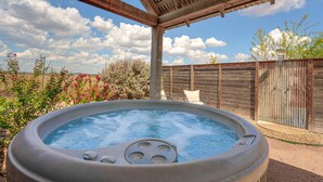 A hot tub under a wooden pergola with a clear sky and a wooden fence in the background.