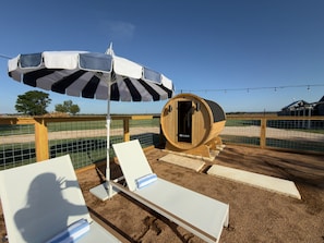 A sauna area with a wooden barrel, two lounge chairs, and a striped umbrella.