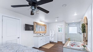 Une chambre moderne avec un grand lit, une coiffeuse avec un miroir, un ventilateur de plafond et une salle de bain avec une baignoire.