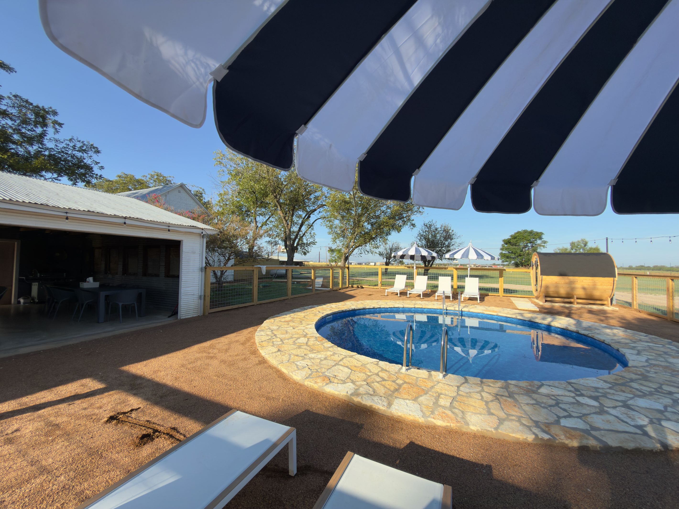 A swimming pool with lounge chairs and umbrellas, surrounded by a fenced area with trees.