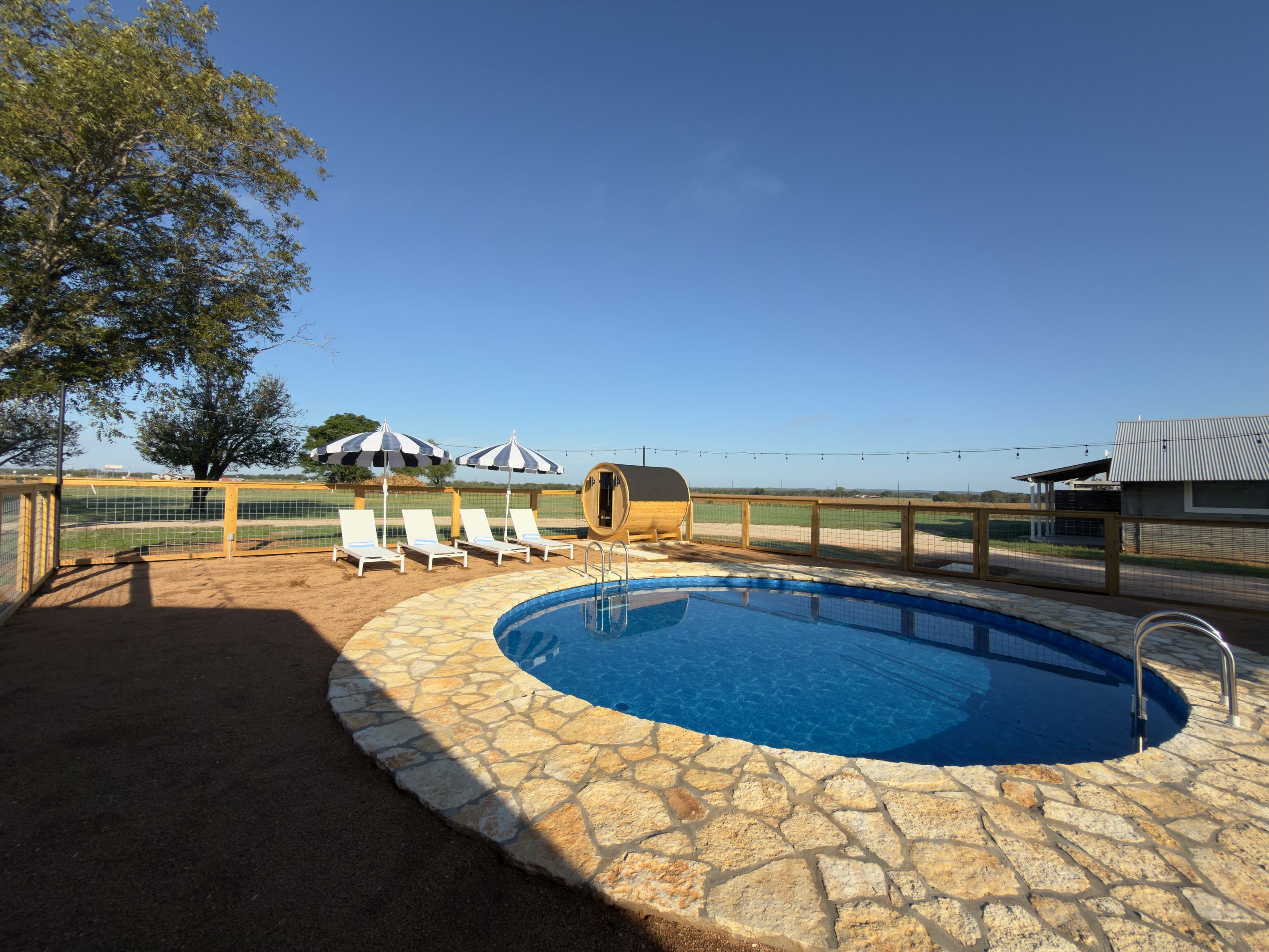 Una piscina con lettini e ombrelloni, circondata da una recinzione e affacciata sul paesaggio.