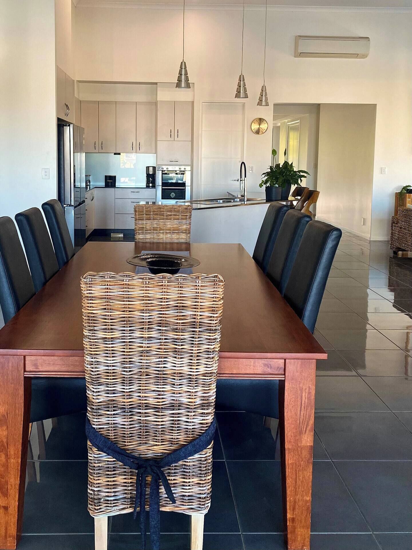 Uma sala de jantar moderna com mesa de madeira, cadeiras estofadas em preto e um centro de mesa tecido.