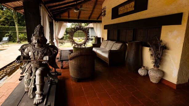 A covered outdoor seating area with a statue, a sofa, and two vases.
