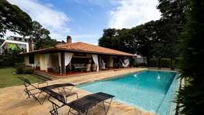 A swimming pool with lounge chairs, a covered patio, and a house in the background.