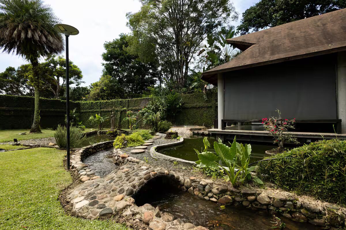 Un jardin aménagé avec un bassin, un sentier en pierre et un bâtiment doté d’un toit foncé.