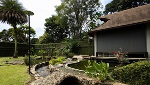 A landscaped garden with a pond, stone pathway, and a building with a dark roof.