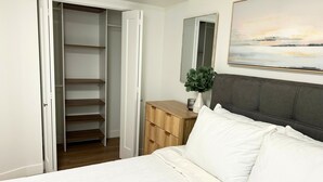 Un dormitorio con cama, mesita de noche, cómoda, armario y un cuadro en la pared.