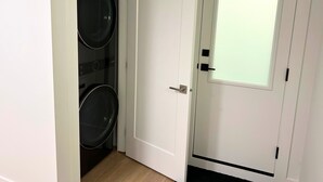 Una habitación con una puerta blanca, un ventanal con vidrio esmerilado y una lavadora.