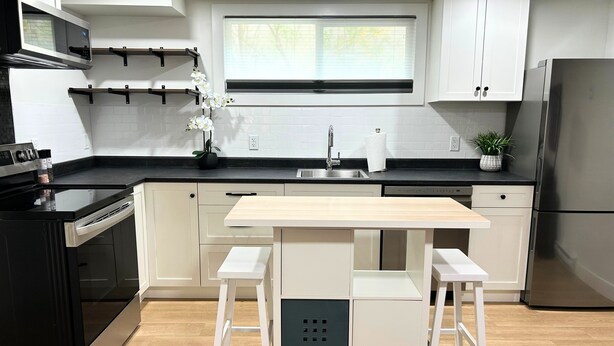 Una cocina moderna con armarios blancos, encimera negra, refrigerador de acero inoxidable y una mesa de comedor de madera.