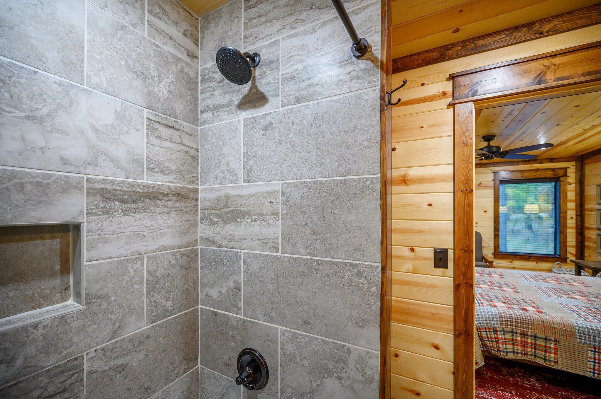 A bathroom with stone tiles, a shower, and a wooden cabin interior with a bed.