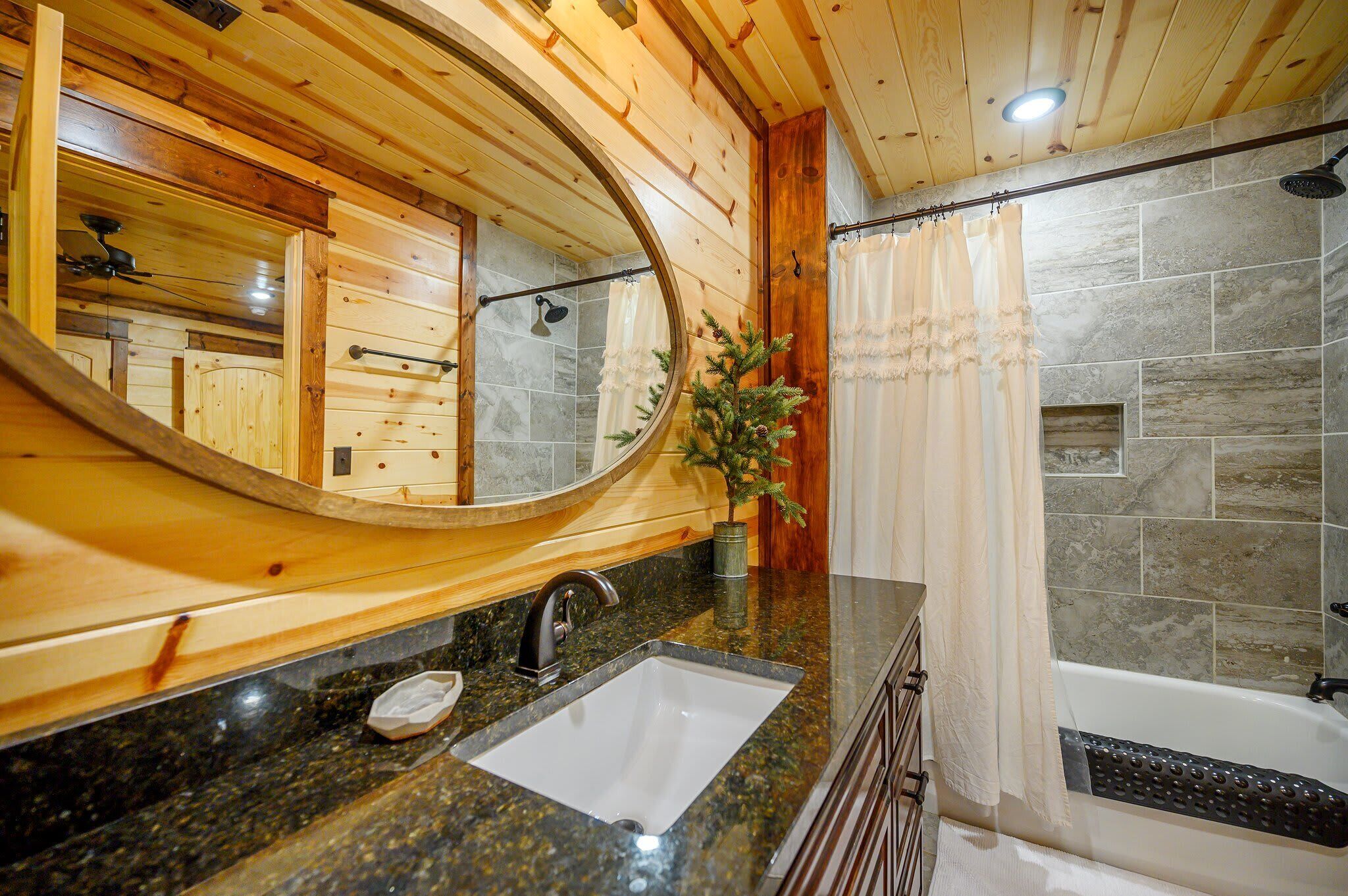 Un baño con tocador de madera, lavamanos, ducha con azulejos de piedra y un espejo grande.