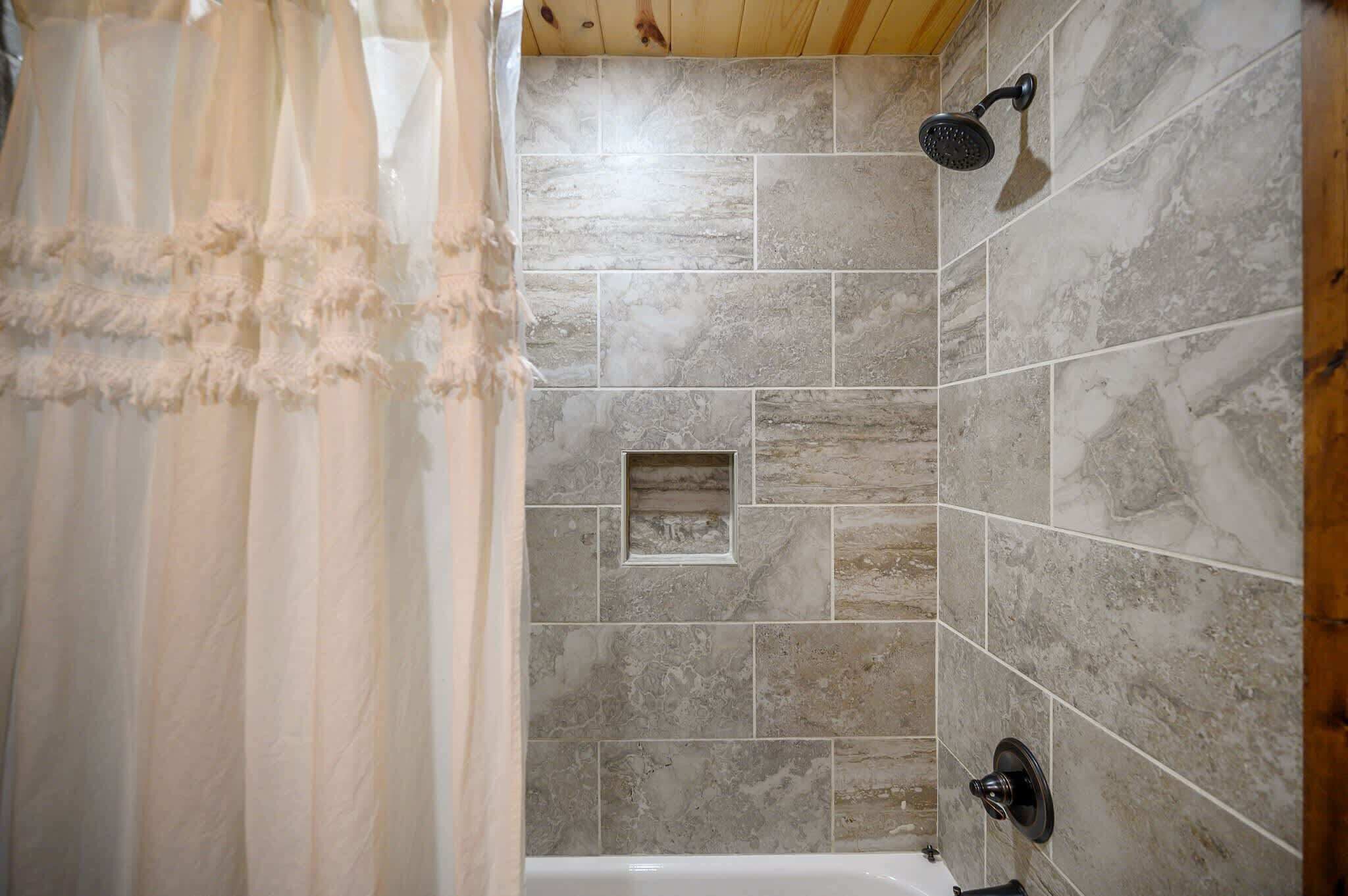 A bathroom with stone tiles, a showerhead, and a small square tile feature on the wall.