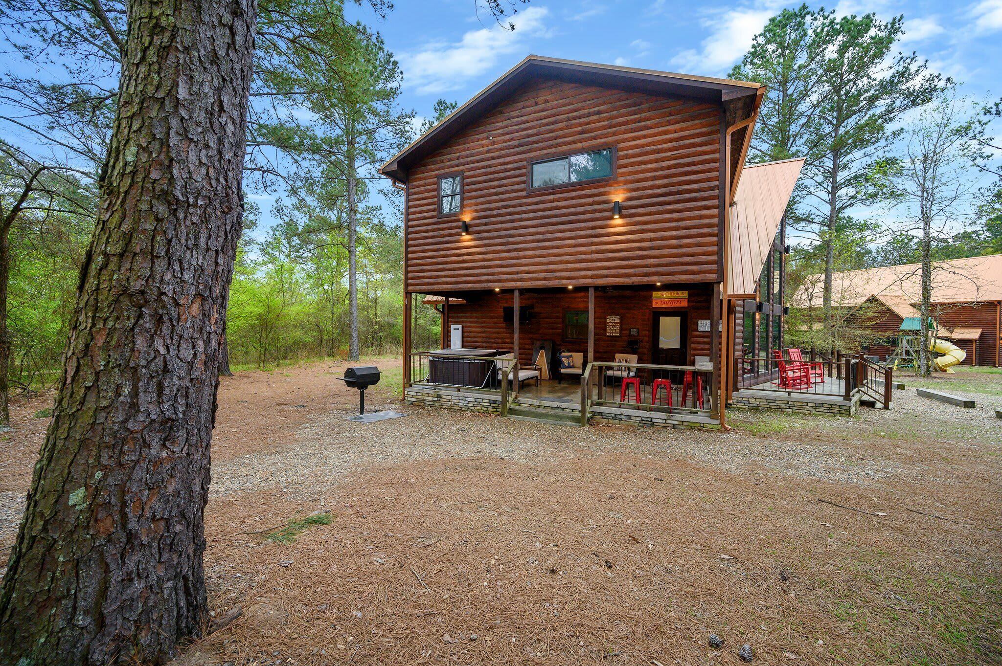 A rustic log cabin with a porch, outdoor seating, and a grill area.