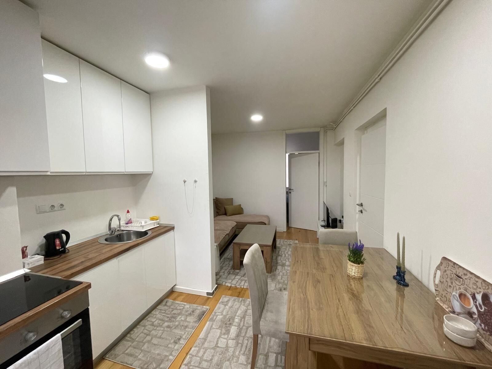 Une cuisine de taille réduite avec des meubles blancs, un évier et une cuisinière. On y trouve également un coin repas avec une table et des chaises en bois.